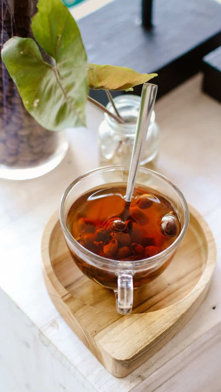 A cup of herbal tea with berries served on a wooden tray, creating a refreshing, warm ambiance.