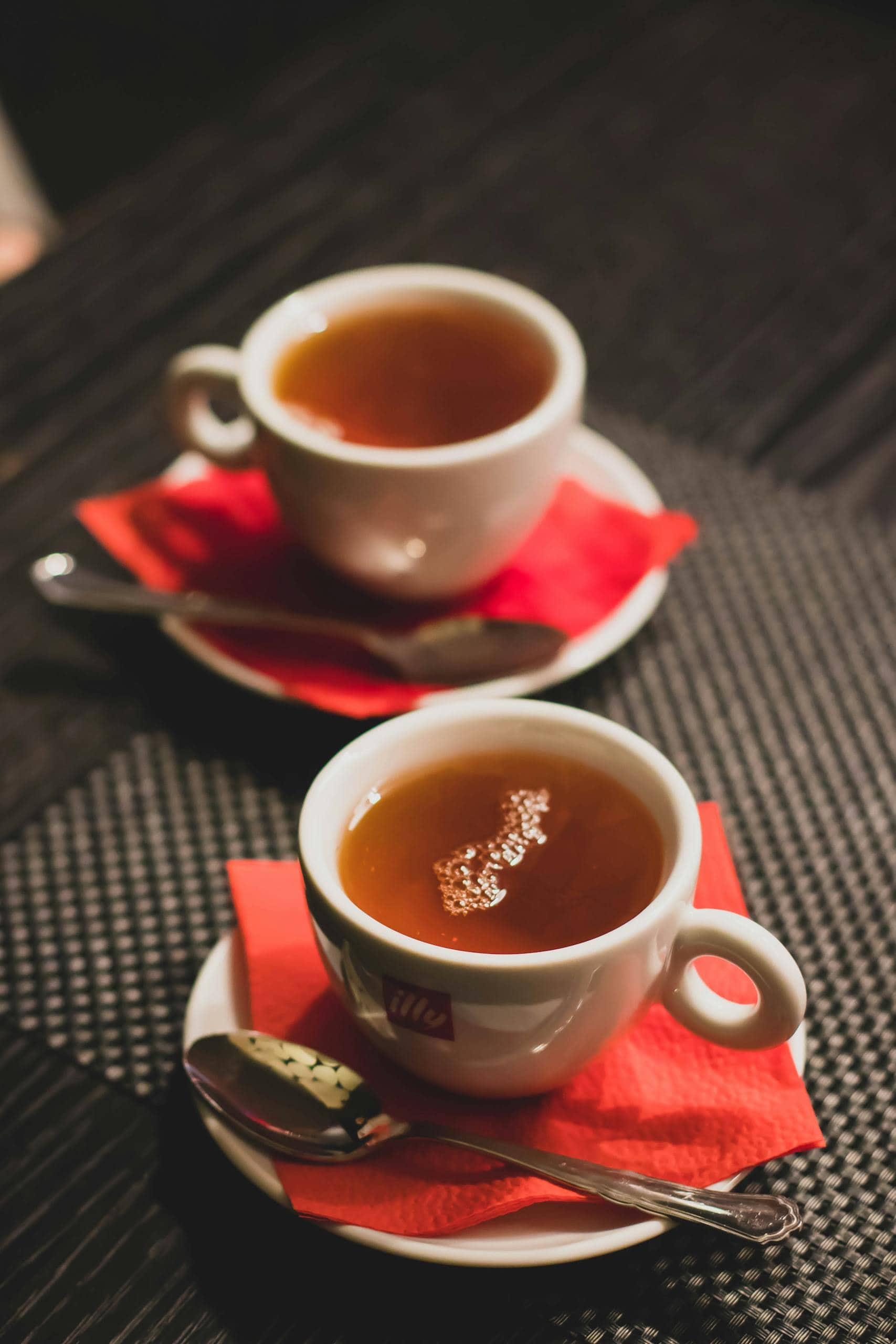 Close-up of two hot teacups on red napkins with spoons, perfect for tea time.